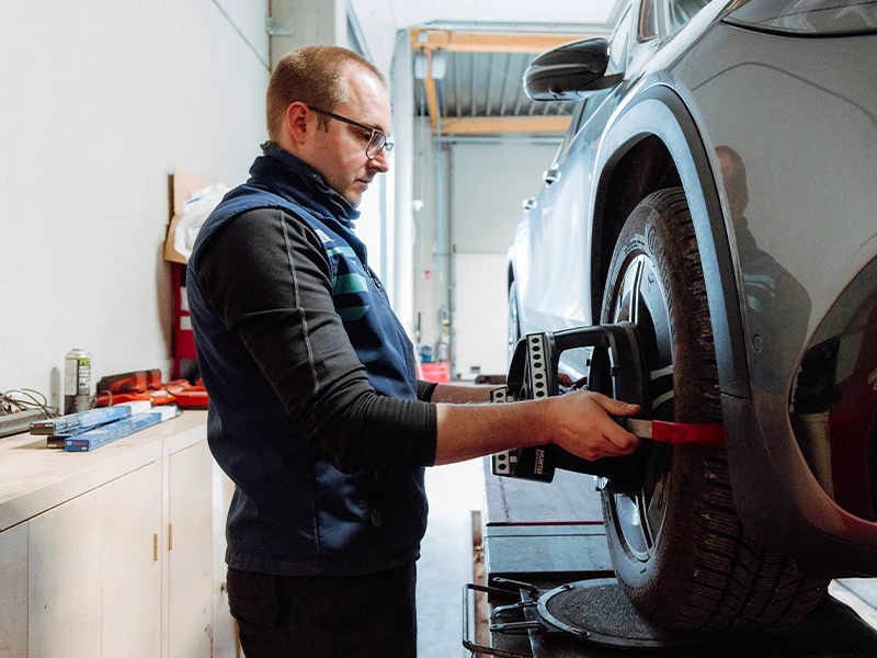 Technicien plaçant un appareil de géométrie sur la roue d’une voiture en atelier.