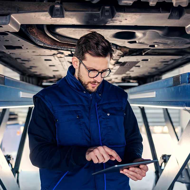 Technicien réalisant un diagnostic mécanique sous un véhicule sur pont élévateur chez Bomerée Pneus.